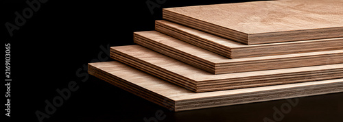 Five plywood sheets stacked in a stepped arrangement against a black studio background, showing natural wood grain and layered veneer edges for construction, furniture, cabinetry, and interior design.