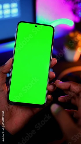Close-up angle of a hand holding a smartphone with a green screen, ideal for video editing.