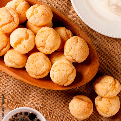Homemade Brazilian cheese bread served on a wooden platter, accompanied by fresh Minas cheese, butter, and black coffee