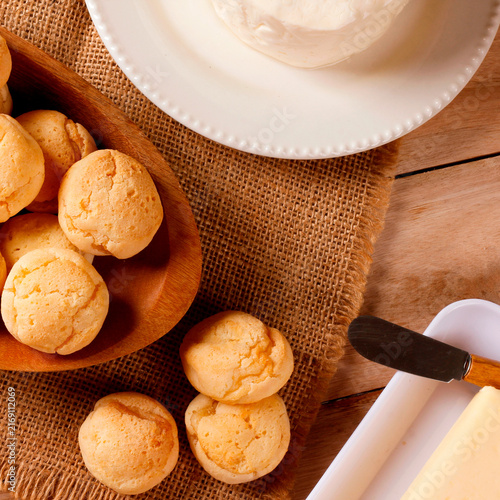 Homemade Brazilian cheese bread served on a wooden platter, accompanied by fresh Minas cheese, butter, and black coffee