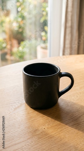 Black coffee mug on a wooden table near a window with soft light.
