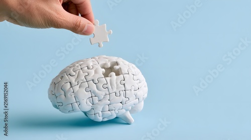 Hand placing the last jigsaw puzzle piece into a white brain model, mental health, memory care, problem solving, psychology, neuroscience, dementia awareness and completing the thinking process