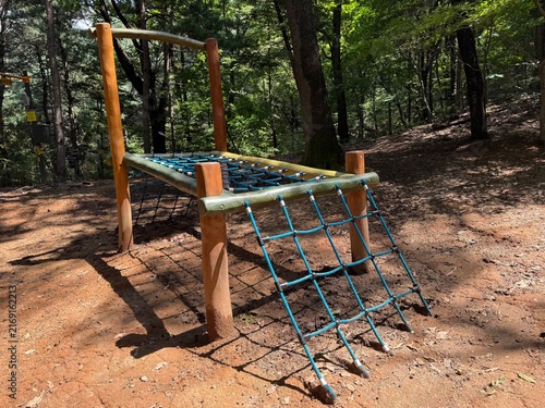 Wooden rope bridge and playhouse at shaded outdoor forest playground