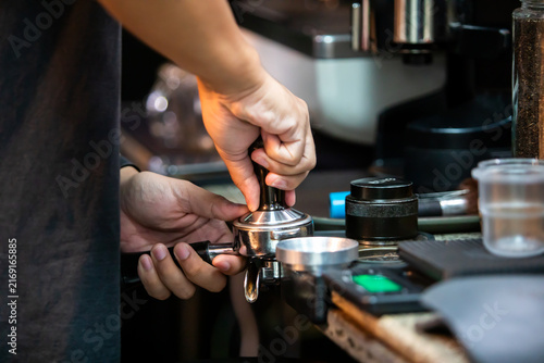 фотографія Selective focus to professional barista using a hand tamper to press ground coffee powder in a portafilter at a coffee shop counter to prepare fresh espresso