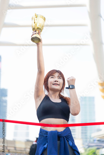 A beautiful, fit woman holds a victory trophy in the middle of the city; a concept promoting health.