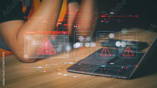 Programmer working on laptop with red warning alert icons displaying coding error, system failure, software bug, and cyber security threat on virtual digital screen interface in dark office.