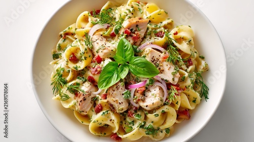 Creamy tortellini pasta salad with grilled chicken, red onion, and fresh basil on white background