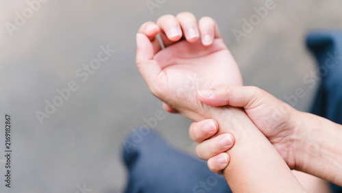 Unrecognizable man gripping his painful wrist joint outdoors. Illustrating carpal tunnel syndrome, peripheral neuropathy, hand numbness, office syndrome, and chronic joint inflammation.