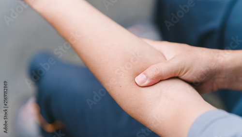 Close up of an adult massaging his sore forearm muscle outdoors. Concept of physical arm fatigue, repetitive strain injury, tendonitis, sports trauma, and need for physical therapy care.