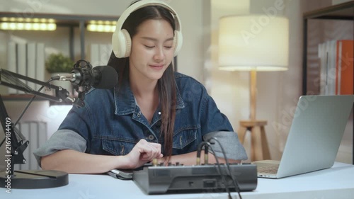 Podcast digital creator home studio woman with headphone and microphone on laptop at tidy desk, focused recording talk show and calm voice content, warm lamp light, cozy room audio edit and guidance