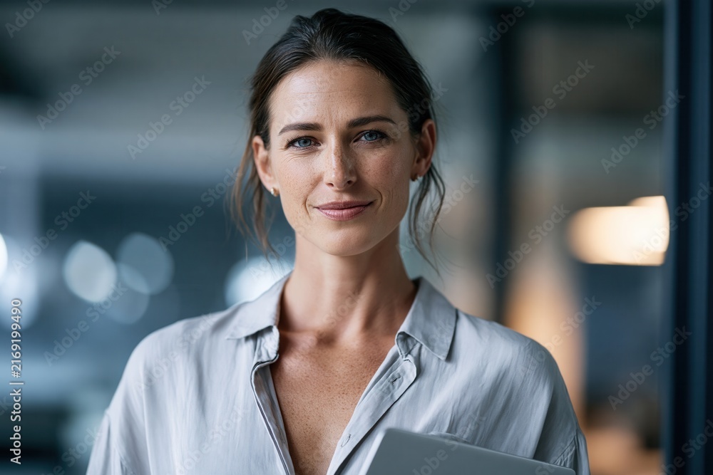 Obraz premium Smiling businesswoman holding a laptop in a modern office.