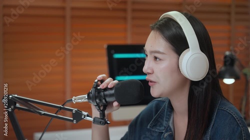 Podcast digital creator home studio microphone headphone woman recording clear audio, focused voice at desk, warm lamp light, wood blind backdrop, cozy modern workspace, calm talk, smiling