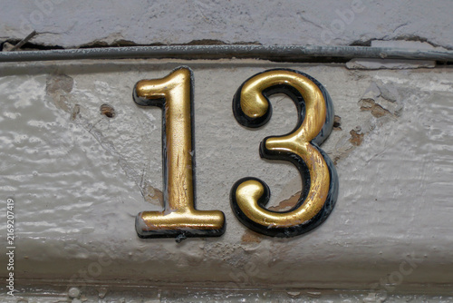 House number thirteen in vintage golden metal letters on old cracked wall