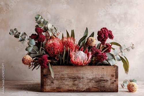 Floral arrangement in wooden box featuring protea, eucalyptus, and other flowers, creating a beautiful and elegant display.