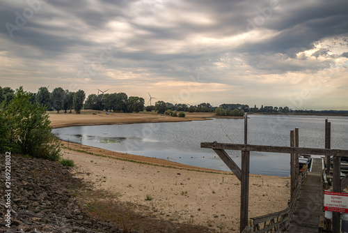 Foto Der See lag ruhig unter dem dramatischen Wolkenhimmel, während die Sonnenstrahlen wie goldene Finger durch die Wolkendecke griffen