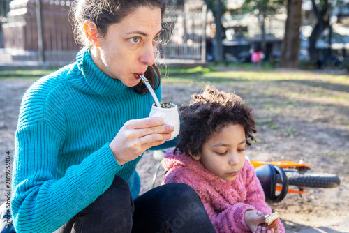 Mother and interracial daughter drinking mate in argentina park