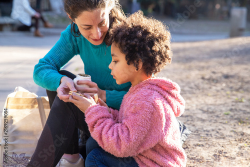 Multiethnic mother and daughter sharing mate and cookies in public park.