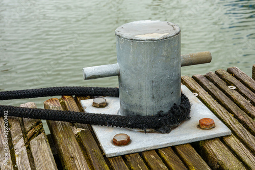 Foto Metal bollard securing boat with rope on wooden pier