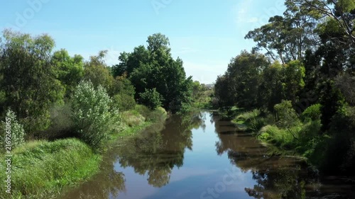 Peaceful river flows through lush green Australian bushland on sunny day.
