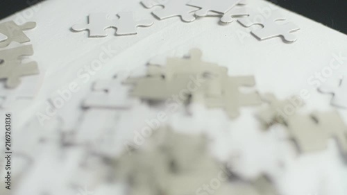 Cinematic macro shot of scattered white puzzle pieces on clean surface featuring smooth camera motion and soft lighting.