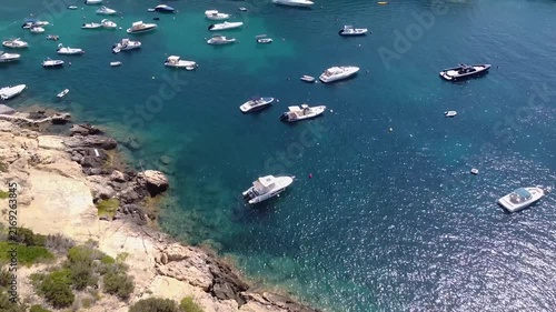 Aerial view of motorboats and yachts anchored in turquoise mediterranean bay on sunny day.