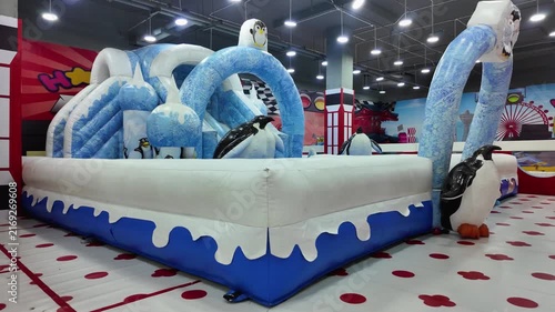 Large inflatable bouncy castle and slide playground with winter arctic penguin theme in indoor children amusement center.
