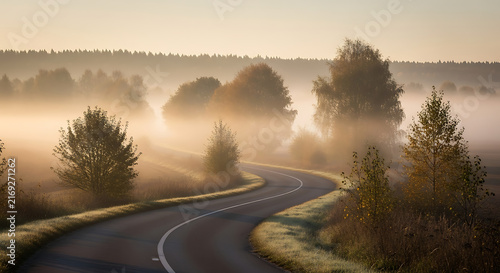 A winding country road curves through a misty forest landscape during a golden sunrise morning with rural landscape filled