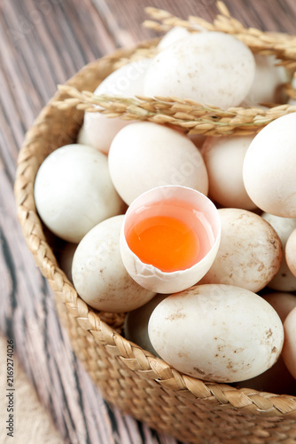 Obraz na płótnie Fresh Duck Eggs in Rustic Wicker Basket with Cracked Shell and Orange Yolk on Wo