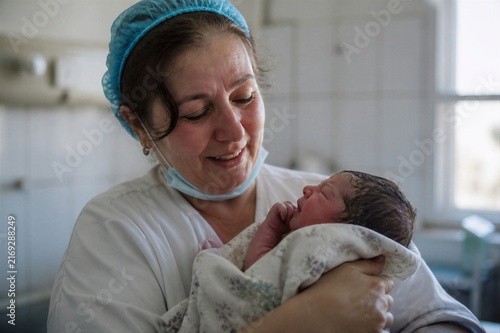 Smiling woman midwife holding a newborn baby after delivery. Compassionate maternity healthcare and birth support in a hospital setting.