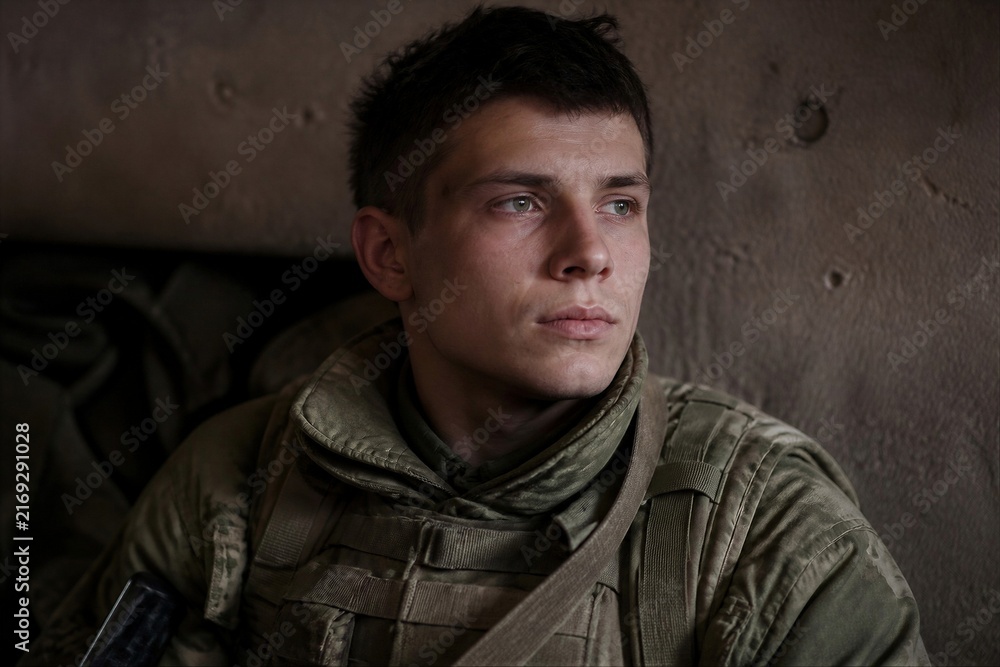 Obraz premium Stoic young soldier in military uniform and protective gear staring ahead. Documentary portrait expressing duty, courage, resilience, war, and service with dramatic copy space.