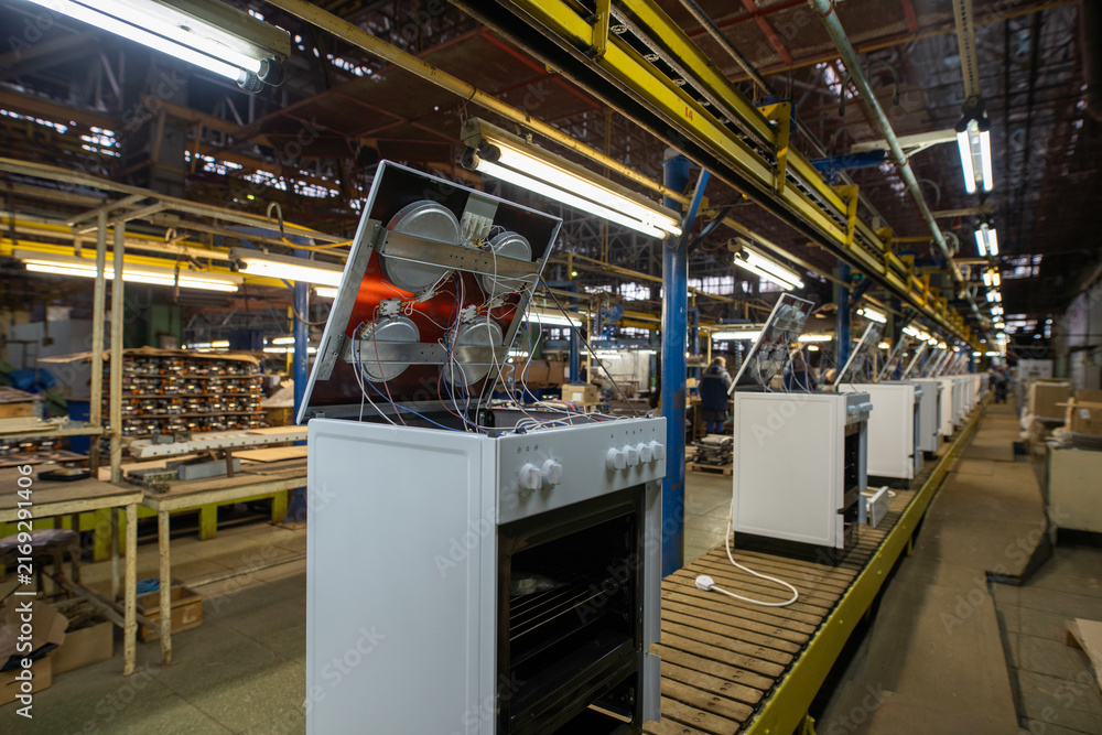 Fototapeta premium Factory assembly line with white ovens on conveyor belt under industrial lighting