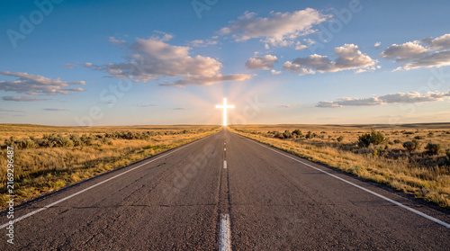 A radiant glowing cross stands at the horizon of a straight road through open prairie under a vast blue sky