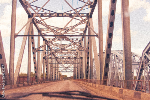 Cinematic vintage illustration from inside a steel truss bridge looking down empty road