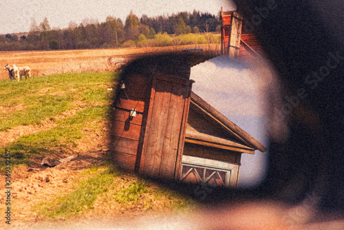 Cinematic vintage illustration with reflection of an old wooden village house in car side mirror