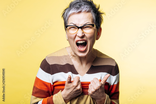 Woman with gray hair screaming, expressing anger and frustration. She is feeling upset, emotional, stressed, and experiencing stress