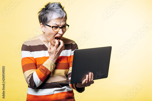 Elderly woman with short grey hair and glasses expressing shock and frustration while looking at a laptop computer