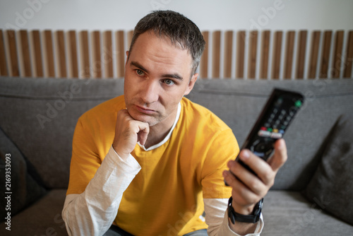 Foto Sad man sitting on a couch holding a remote control, with a tired and disappointed expression