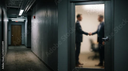 Two businessmen shaking hands behind a closed frosted glass office door