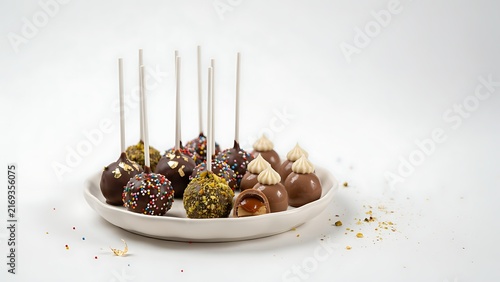 Assorted chocolate cake pops and truffles with sprinkles, gold leaf, and caramel on a white plate