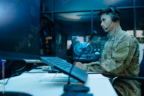 Military operator with headset analyzes radar HUD screens and takes notes in high tech center, ensuring strategic cyber