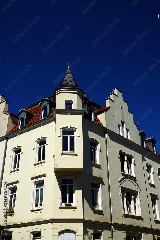 Obraz premium Schönes saniertes altes Eckhaus in Beige und Naturfarben mit Erker und Treppengiebel bei blauem Himmel und Sonnenschein in einem Stadtteil von Bielefeld im Teutoburger Wald in Ostwestfalen-Lippe