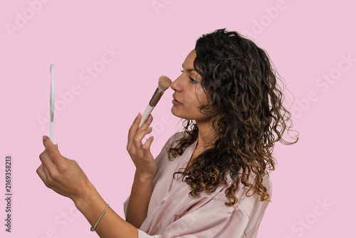 Fotografie Woman applying makeup with brush looking in mirror