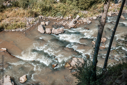 Foto Flowing River Glistens Under the Sunlight Amidst Lush Greenery and Rocky Banks C