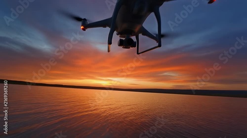 A drone hovers over a lake during a vibrant sunset.