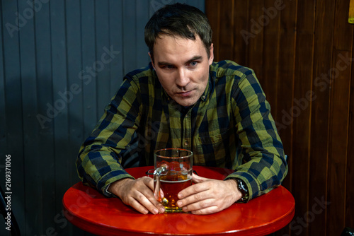 Foto Man sitting alone at a bar with a mug of beer, looking at the camera with a tired, lonely expression