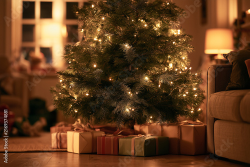 Generative AI - A decorated Christmas tree and wrapped gift under it in a dark sitting room, Christmas time
