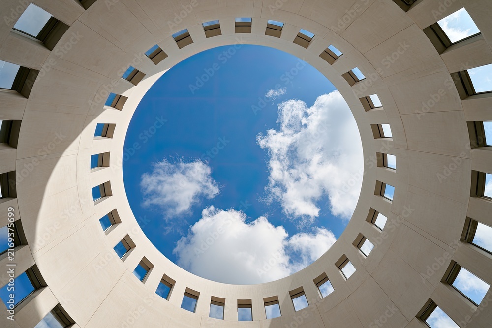 Fototapeta premium Circular building opening framing a bright blue sky with white clouds