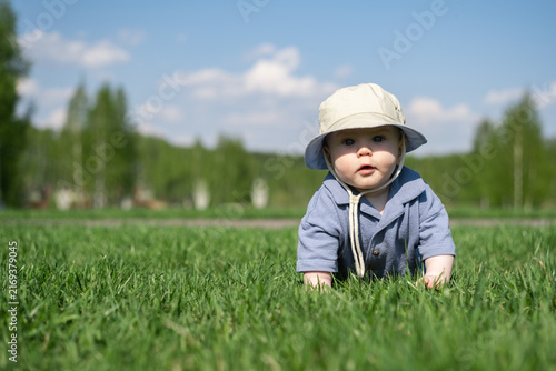 An adorable baby crawls on the green grass outdoors. A little boy is barefoot in the park.