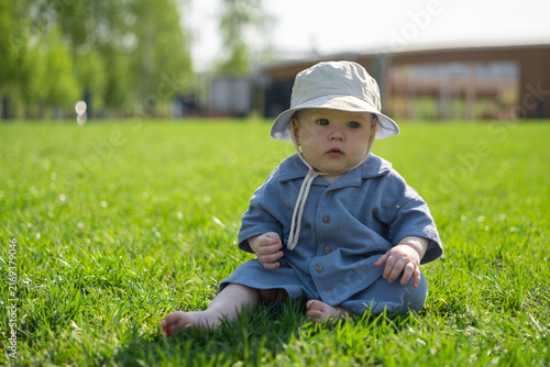 An adorable baby crawls on the green grass outdoors. A little boy is barefoot in the park.