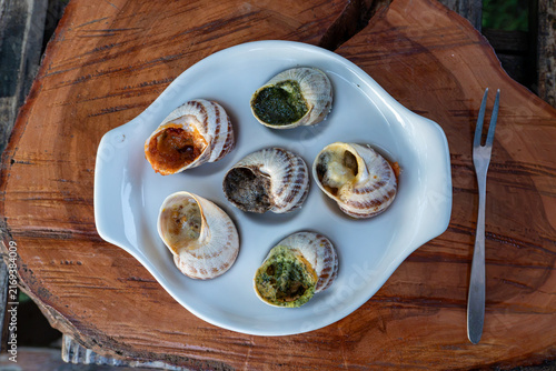 Canvas Print Baked stuffed mollusks are presented with green herb pesto and red spicy tomato sauces inside special white tray on timber background near metal fork outdoors